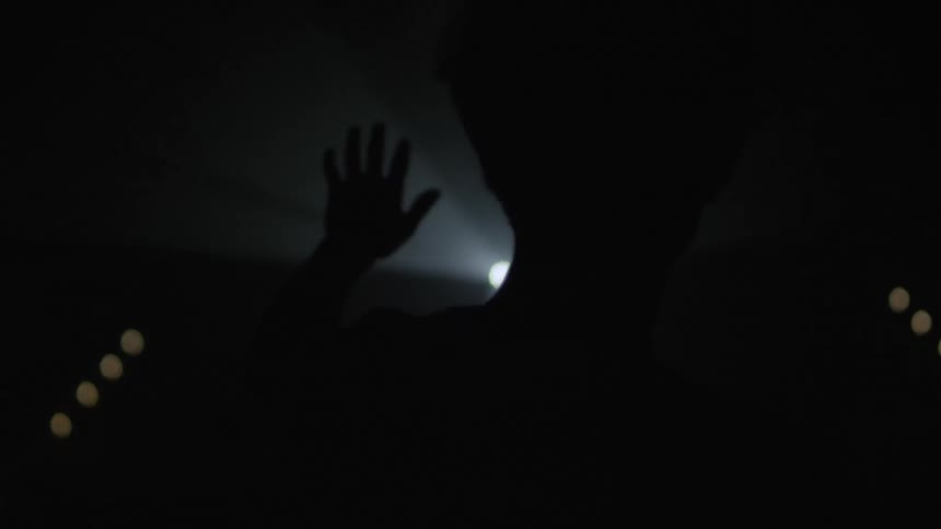 A person in the dark holding up their left hand towards a distant rotating spot light