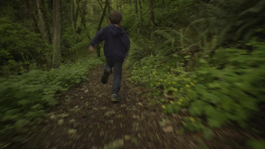 A boy runs fast down a dark path in the woods