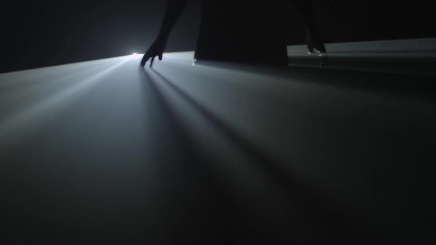 A person moves around in the beams of a strange flashing light behind them