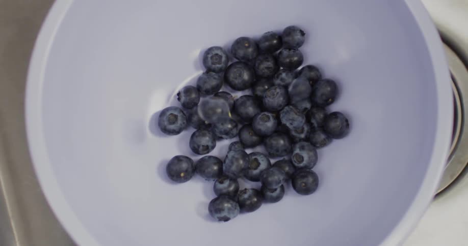 Blueberries drop into a white bowl