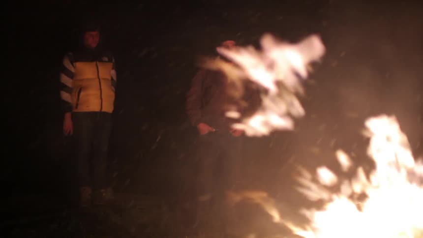 Two men watch a fire burn