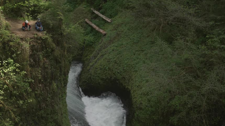 People whitewater kayakers sitting on a cliff above a river and waterfall enjoying a snack before running the river