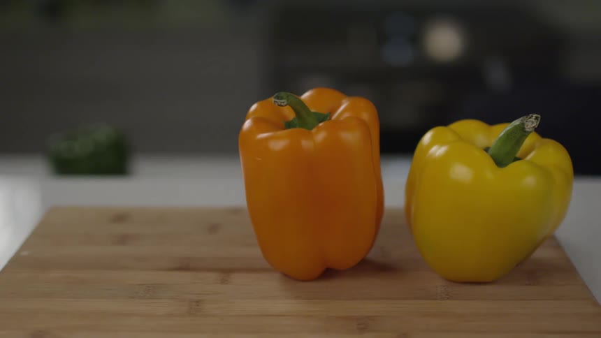 A person sets a yellow, orange and red pepper onto a cutting board