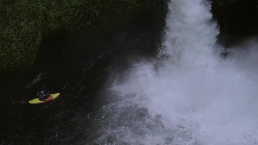 A whitewater kayaker waits at the base of a massive waterfall deep in a wilderness river gorge