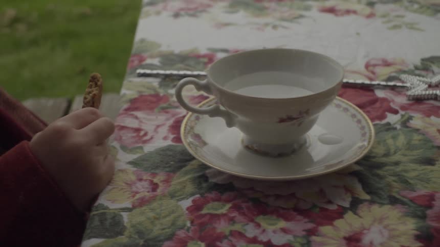 A child eats a cookie in front of a tea cup full of water