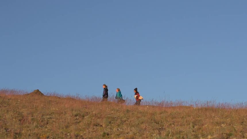 Three people walk up a grassy hill