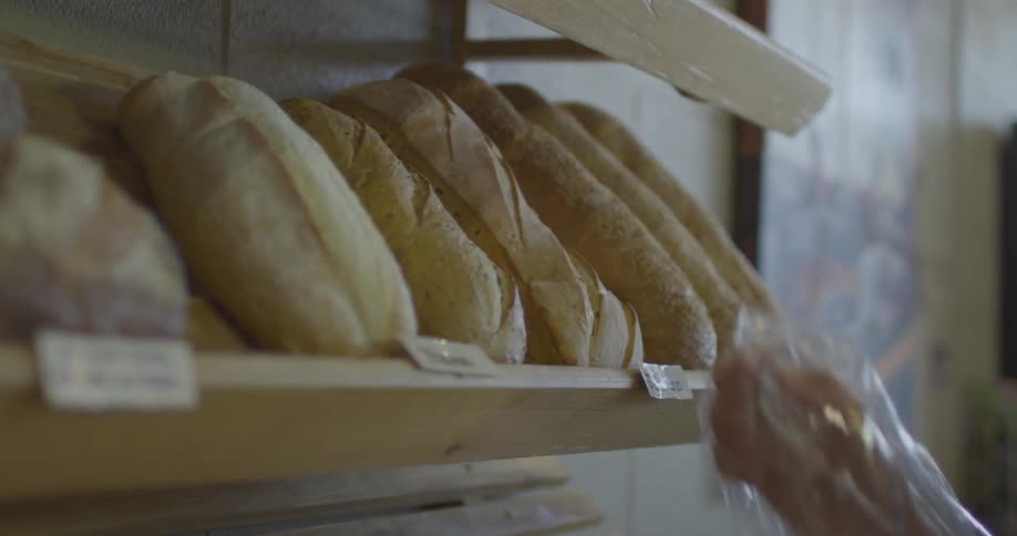 A person with food gloves on places baked bread on a shelf rack on the wall