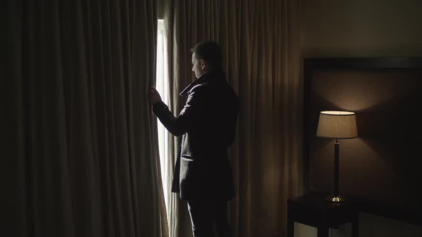 A man peeks outside the window of his hotel room