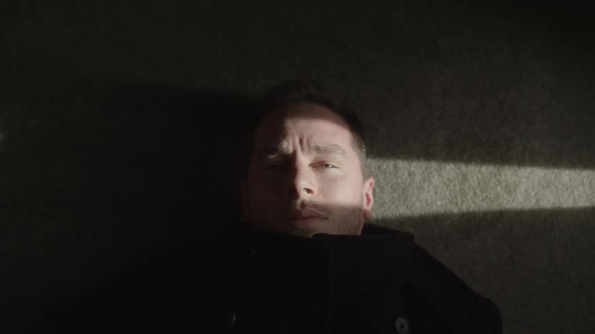 A man lying on the floor opens then closes his eyes