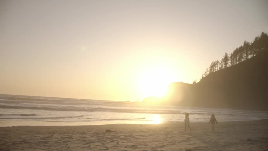 Two children run on a beach at sunset