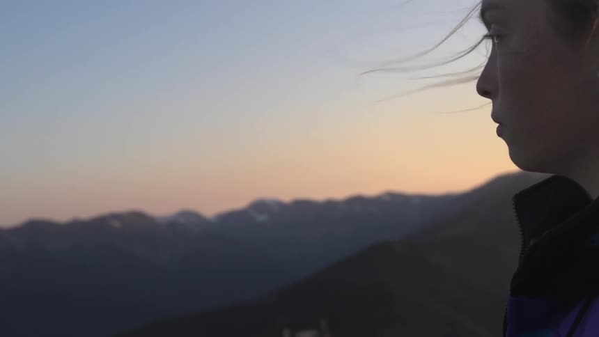 A woman standing outside looking out at mountains during the sunset