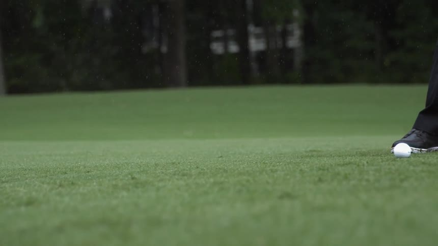 A man hits a golf ball with a club on a green course