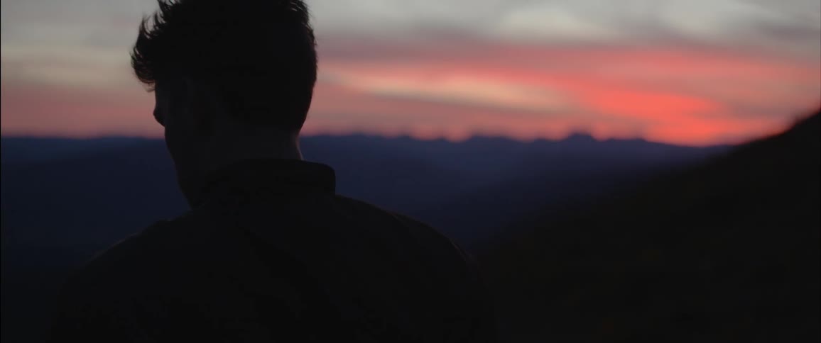 A man is looking out over the mountain range at sunset
