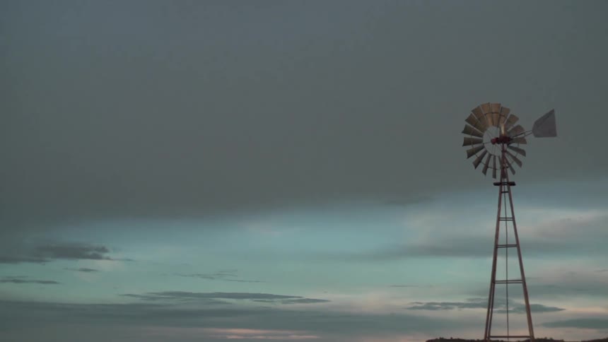 A car parked next to a large windmill in a field at sunset