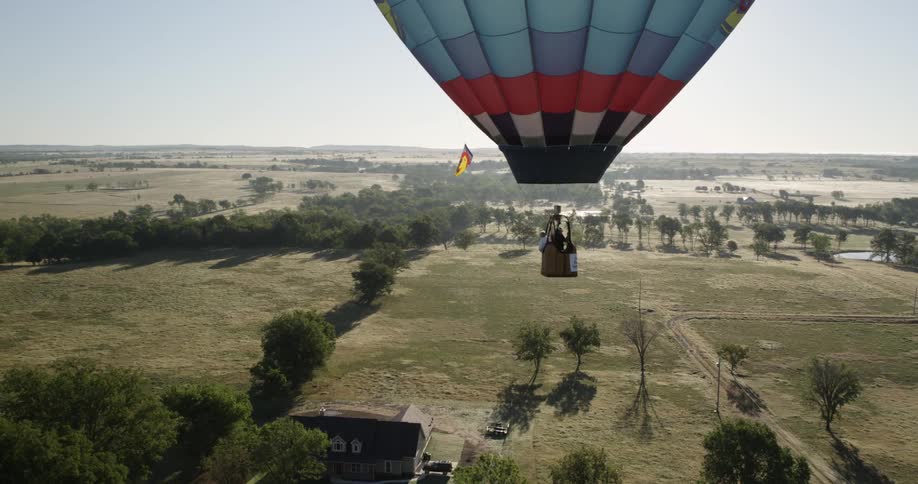 A hot air balloon passing over trees and a home