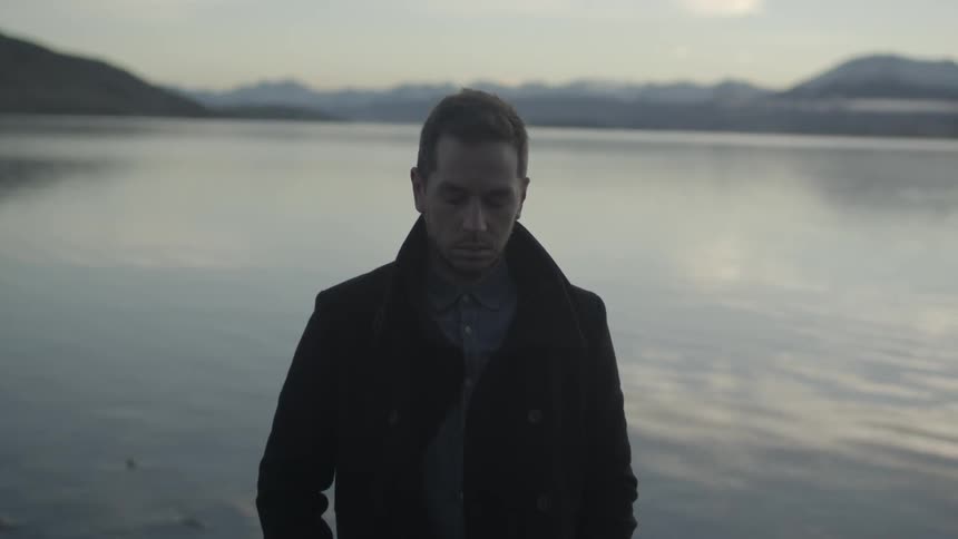 Man standing with his back turned to a lake in the mountains