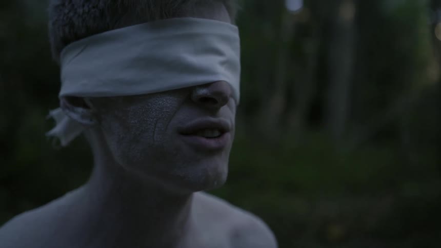 Blindfolded man talking in the woods