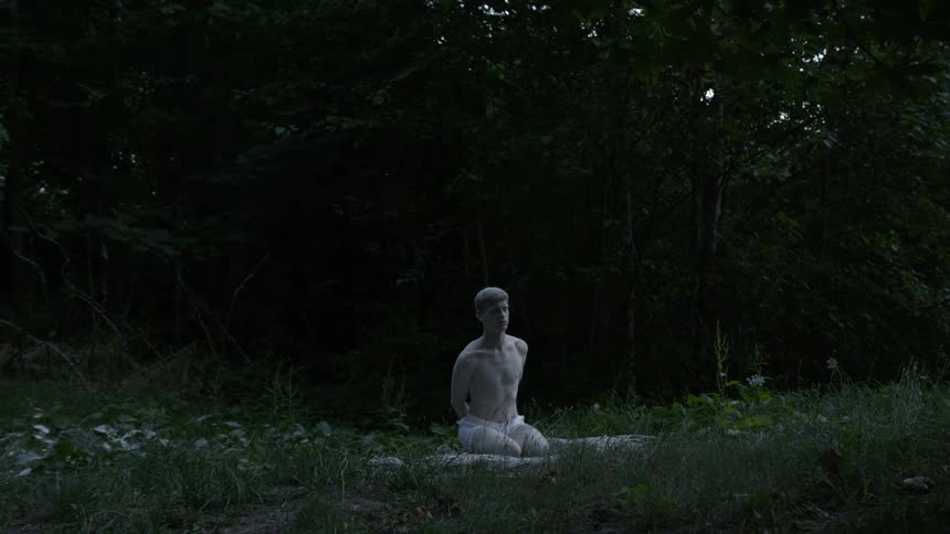 A shirtless man on his knees in the forest