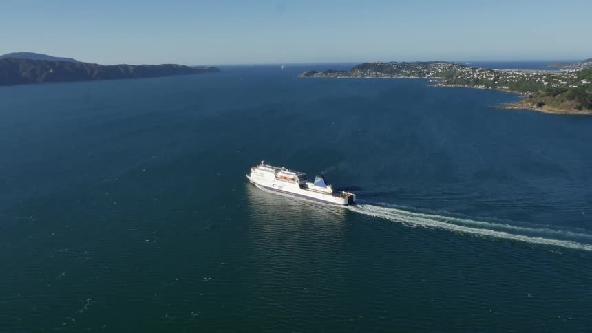 A ship crusing between two hilly land masses that are lined with buildings and trees