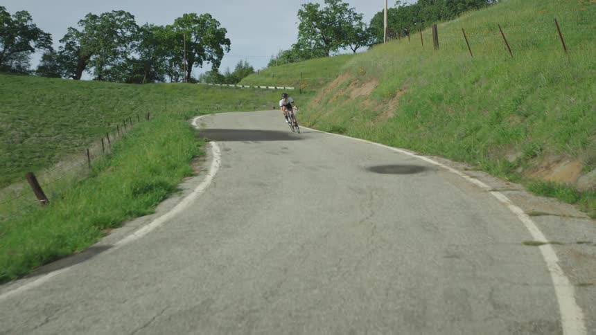 A bicyclist rides a road bike down a winding country road