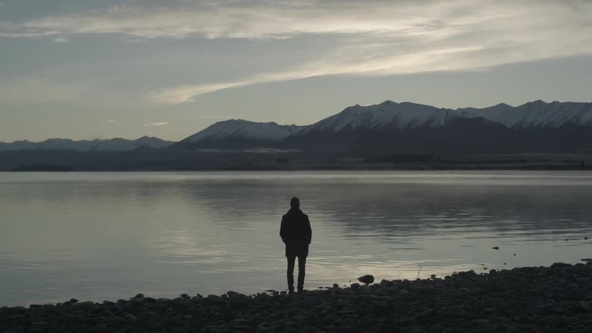 Man stands in front of a lake at dusk