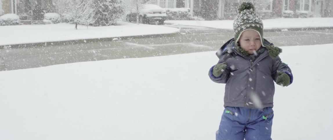 A bundled up toddler walks in the snow