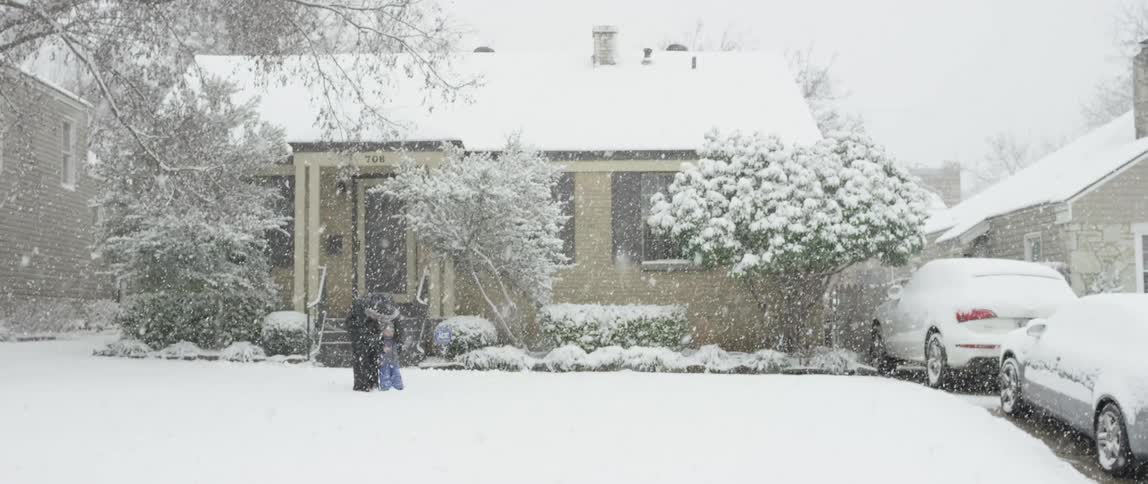 Heavy snow falling, while mother and son play in front of a house
