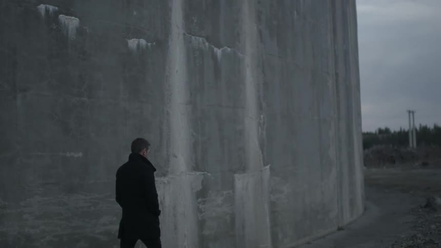 Man walking alongside a tall wall of stone