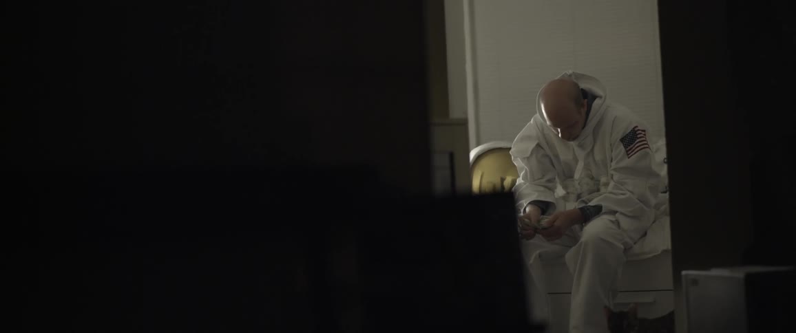 A man dressed as an astronaut sitting on the side of a bed counting money