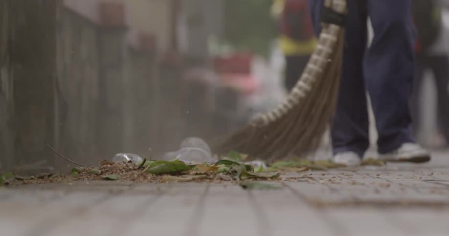 A person sweeping leaves and garbage on a sidewalk near a building