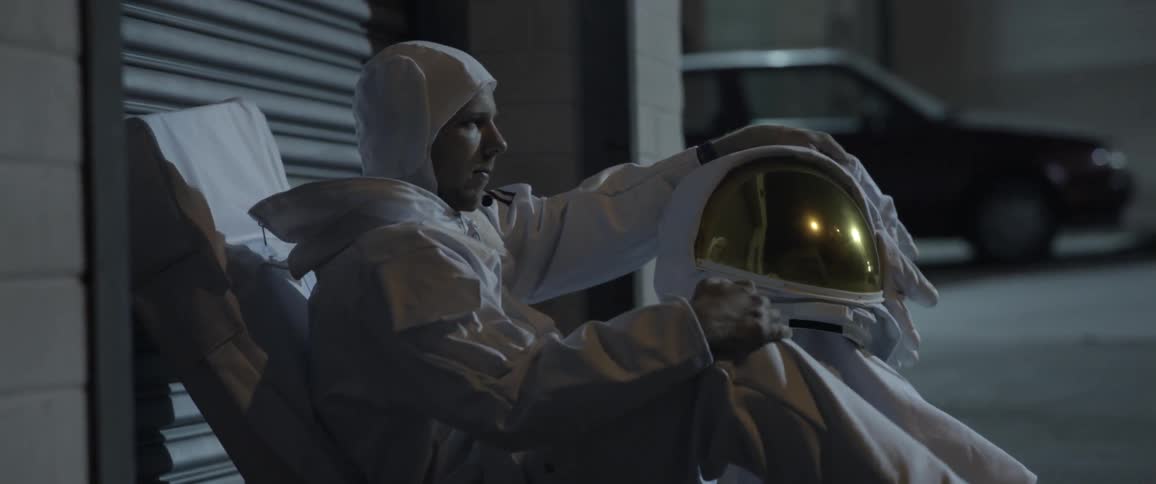 A person wearing a space suit sitting down on the sidewalk
