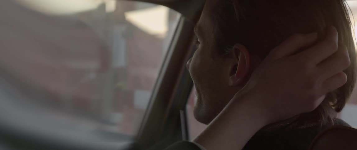 Woman in car runs fingers through man's hair and then they kiss