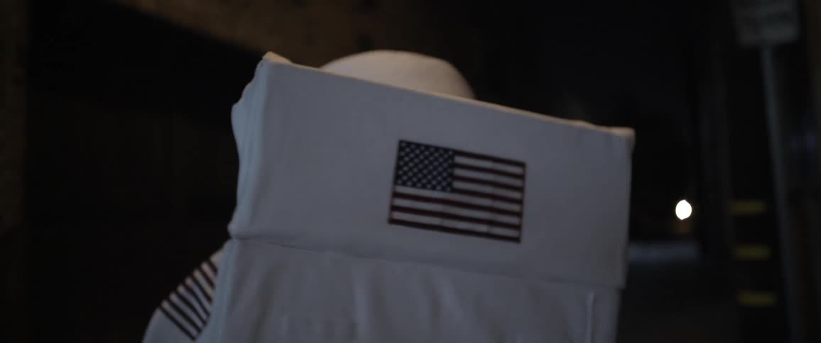 A person in an american spacesuit walks down an alley at night