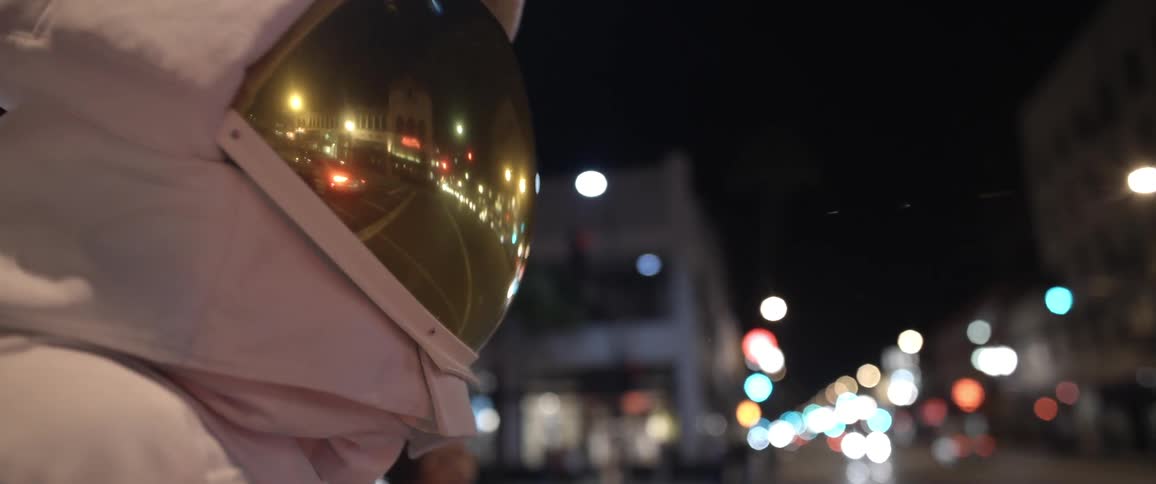 An astronaut stands on a busy city street at night