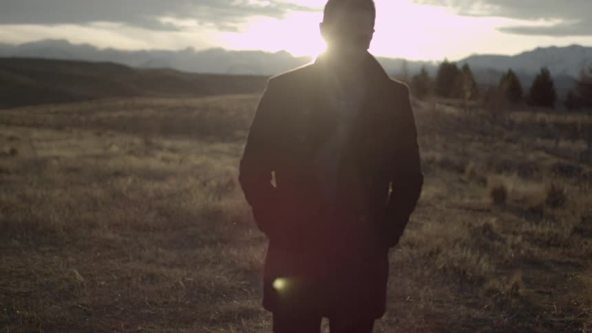 Man walking slowly in a field away from a sunset