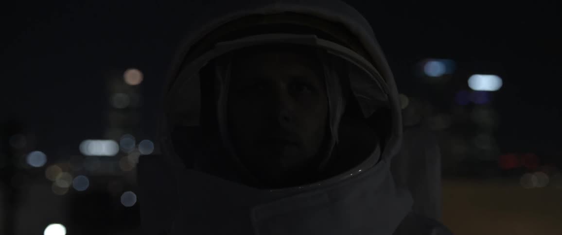 A man in an astronaut suit, face shown, watching flickering lights