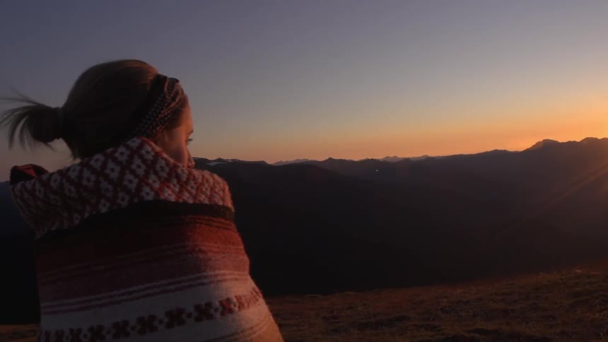 A woman wrapped in a blanket looks towards the sunset