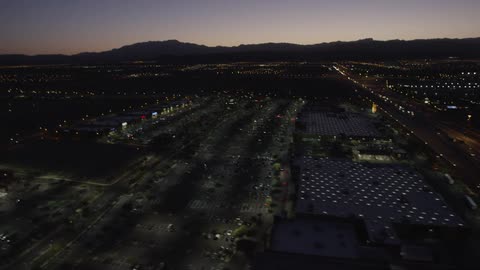 A helicopter view of a city with its lights on during sunset