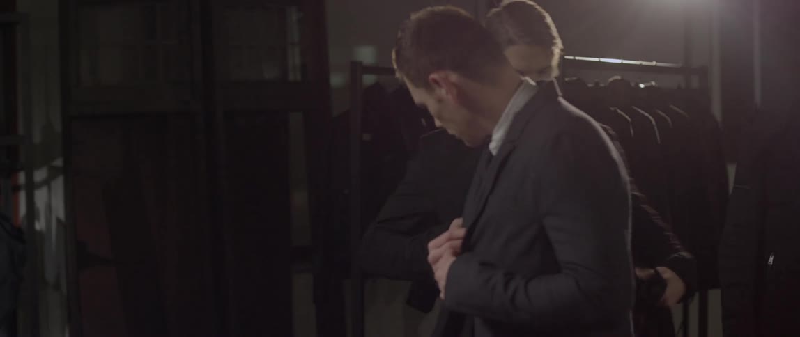 A man tending to his suit and then another man helps him into a coat