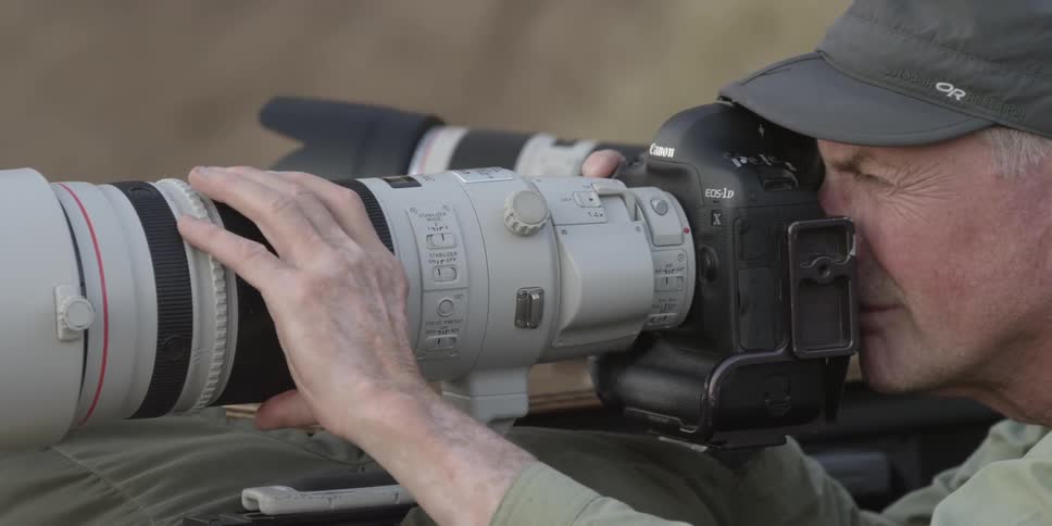 A man holding a camera with a large lens outside