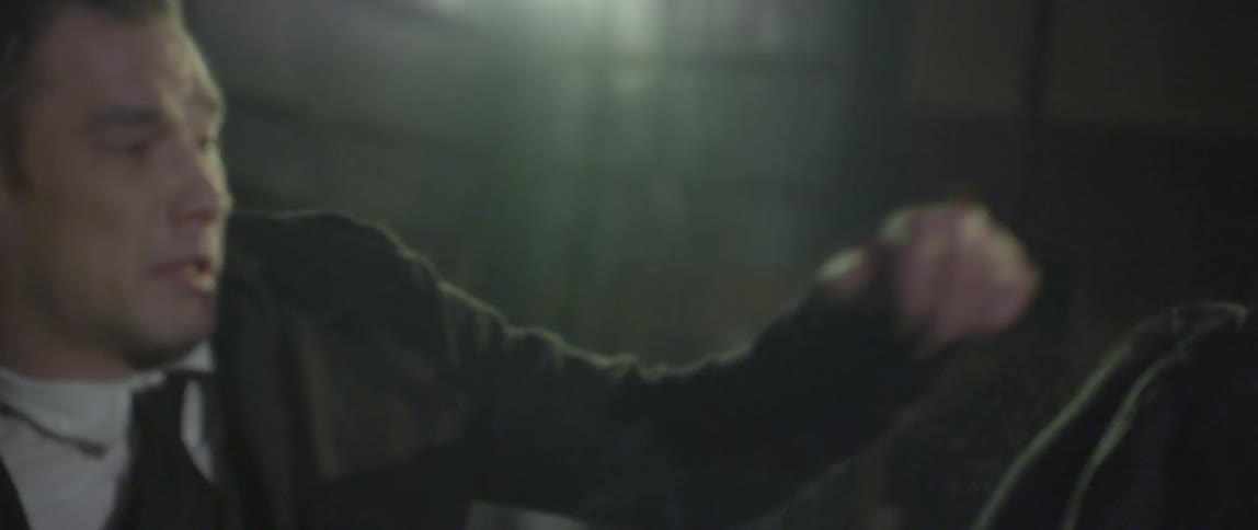 A man in a long black coat fights off attackers