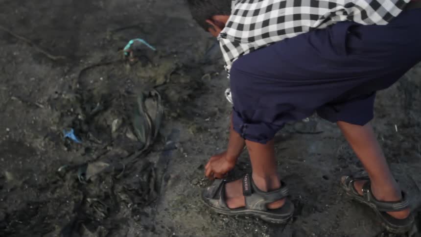A young boy rolls up his pant legs picks up a rock and throws it across a dirt soil terrain