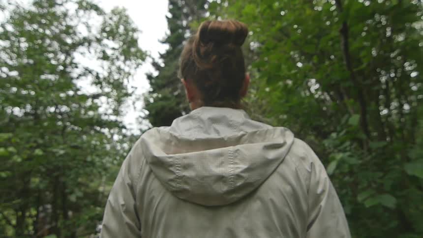 A young woman walks along a path through the woods during the day