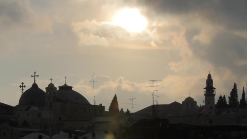 Sun shining through clouds over religious buildings