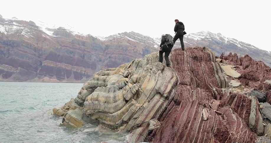 Two hikers climb up a large rock