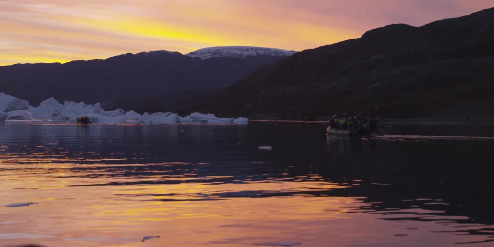 Boaters float near an ice formation at dusk