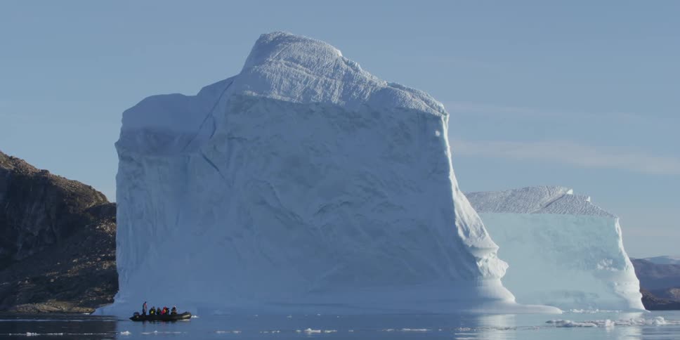 Small boat floating past a very large iceberg