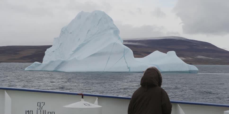 A person on a boat looks at a glacier as it passes by