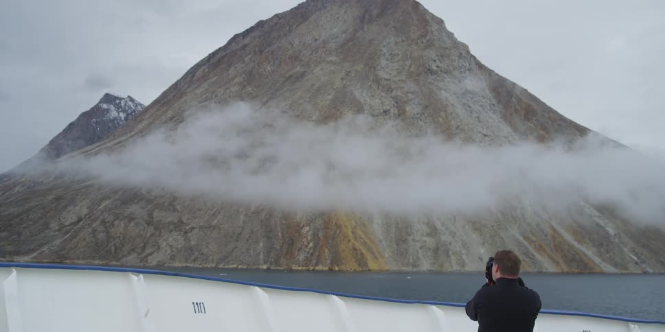 A man takes a picture of a fog covered mountain