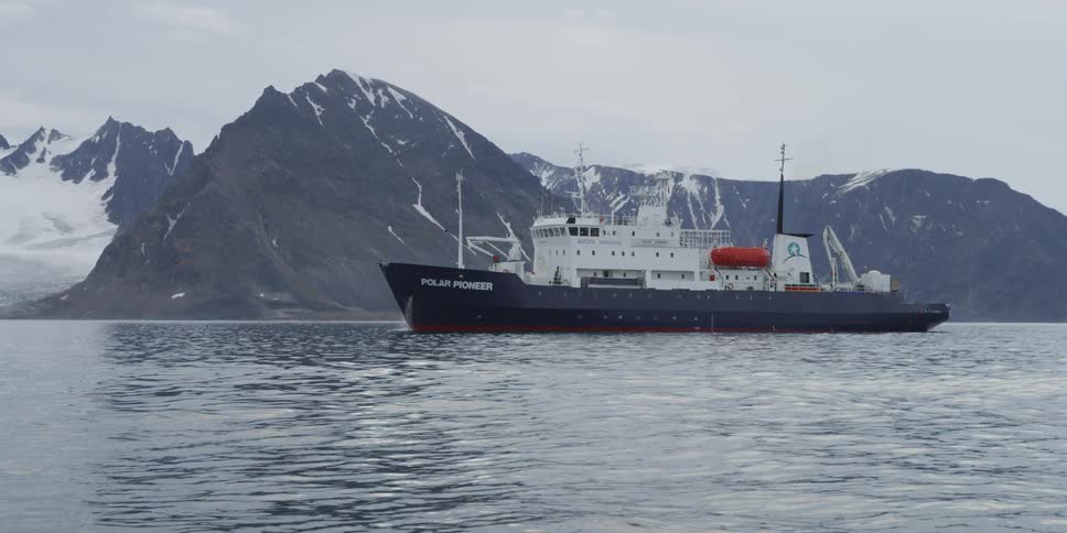 Large ship traveling in water by a mountain